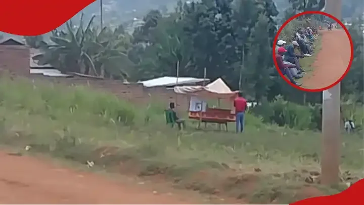 Coffin on table in open field in Metamaywa Kisii with two mourners beside it while crowd sits far on roadside